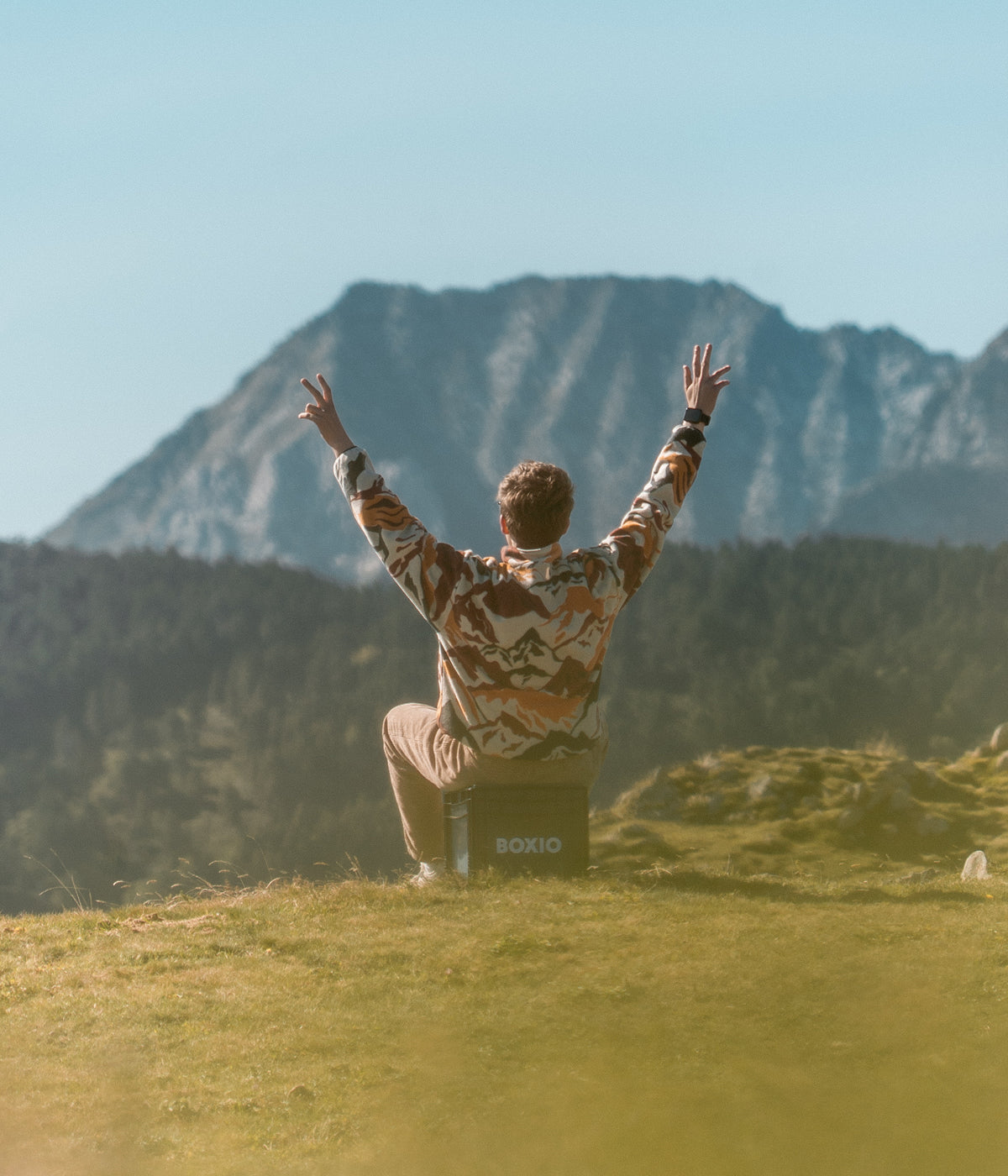 Mann sitzt auf eine Trockentrenntoilette in der Natur und guckt Berge an